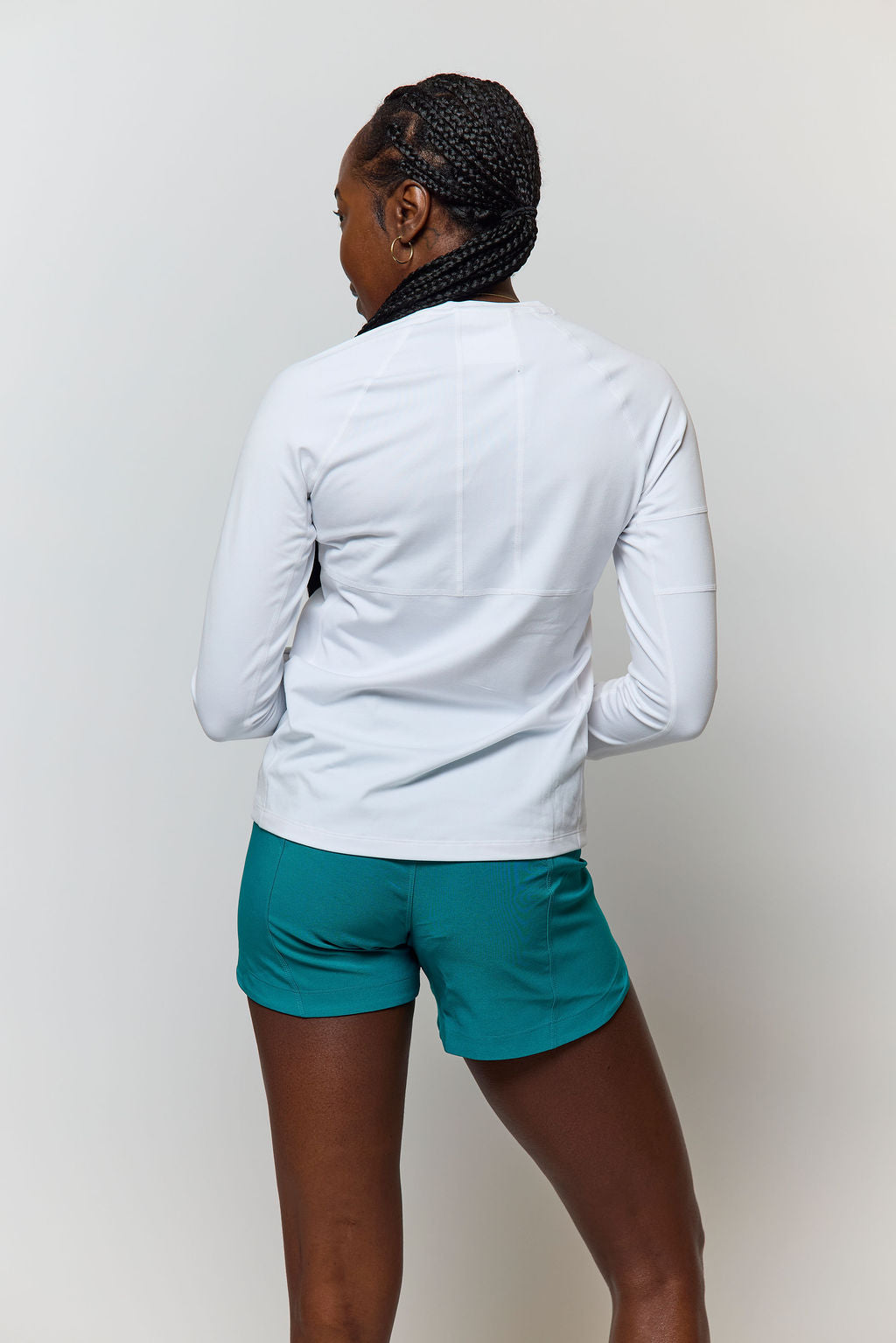 Person wearing a white long-sleeve shirt and teal shorts on a plain background