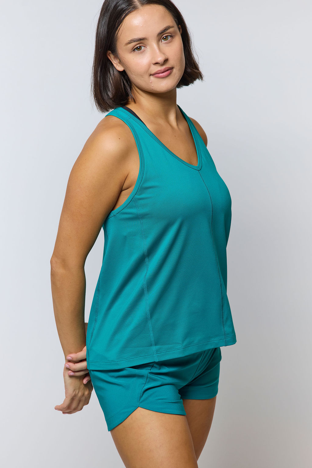 Woman wearing a teal tank top and shorts on a light gray background