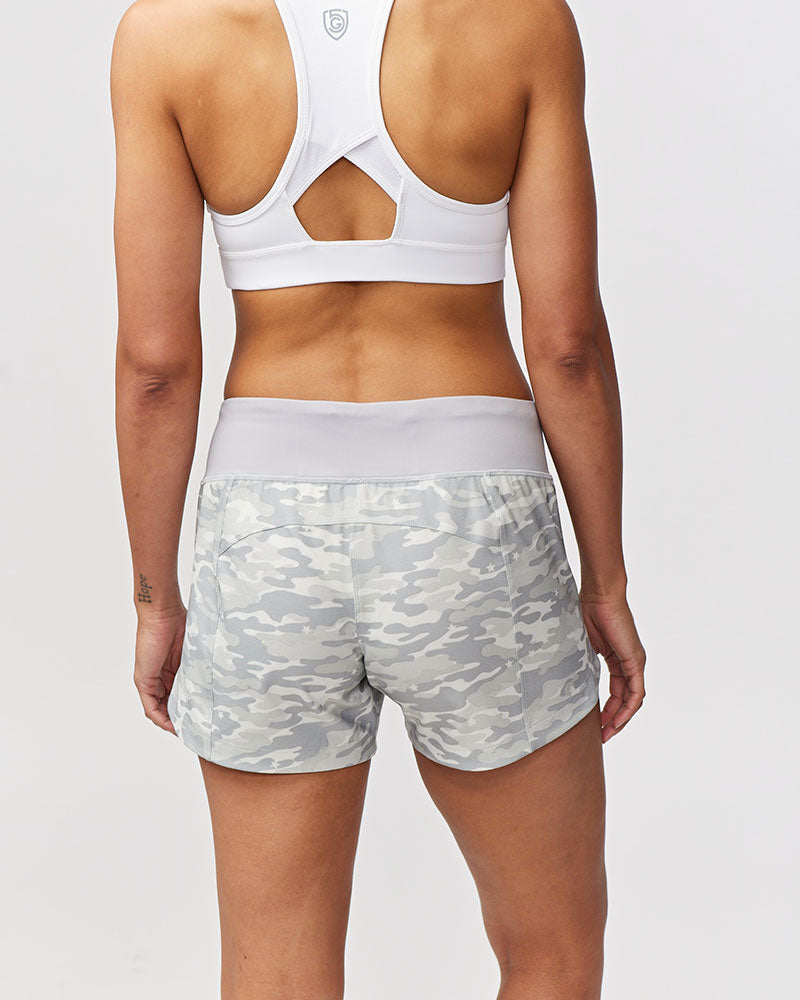 Person wearing a white sports bra and camouflage shorts on a plain background