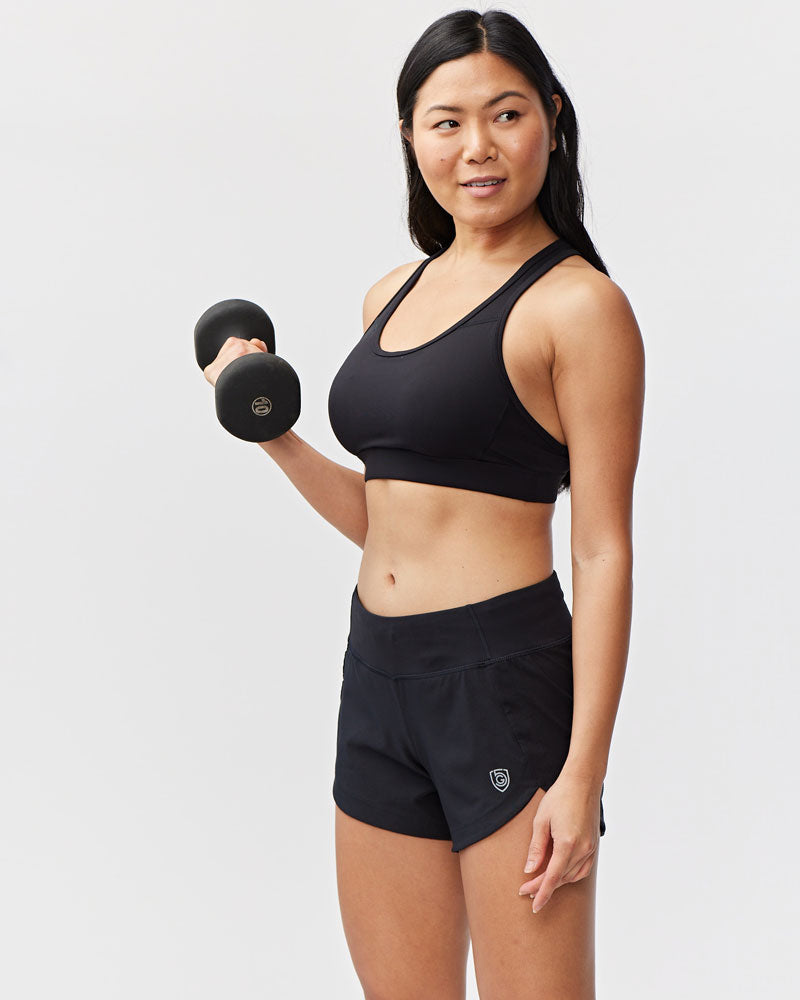 Woman in black athletic wear holding a dumbbell against a light gray background