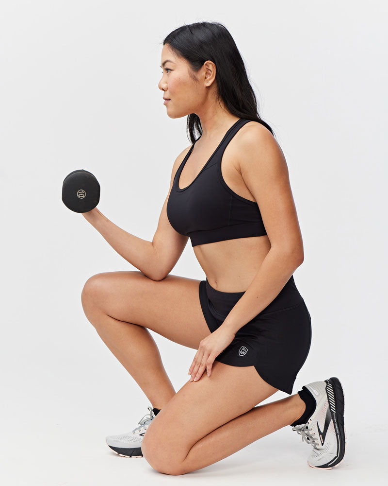 Woman in black athletic wear exercising with a dumbbell on a white background