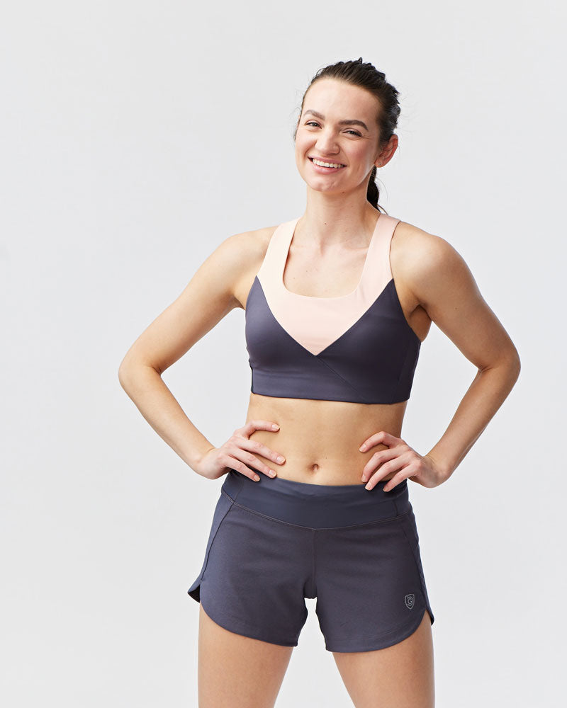 Woman wearing a sports bra and shorts on a plain background