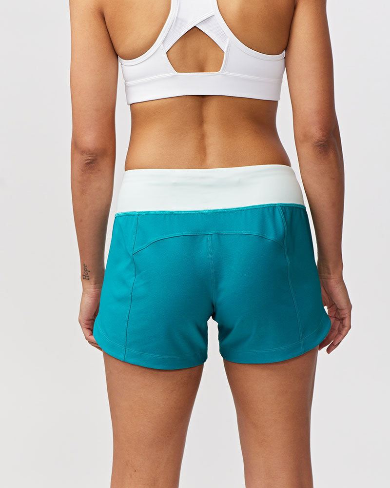 Person wearing a white sports bra and teal shorts on a plain background