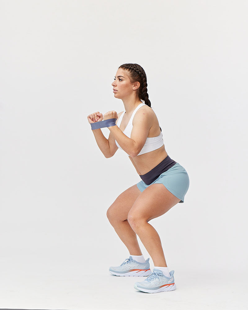 Woman performing a squat exercise with resistance bands on a white background