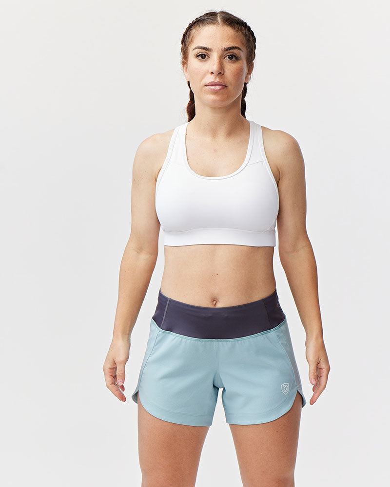 Woman wearing a white sports bra and light blue shorts on a plain background