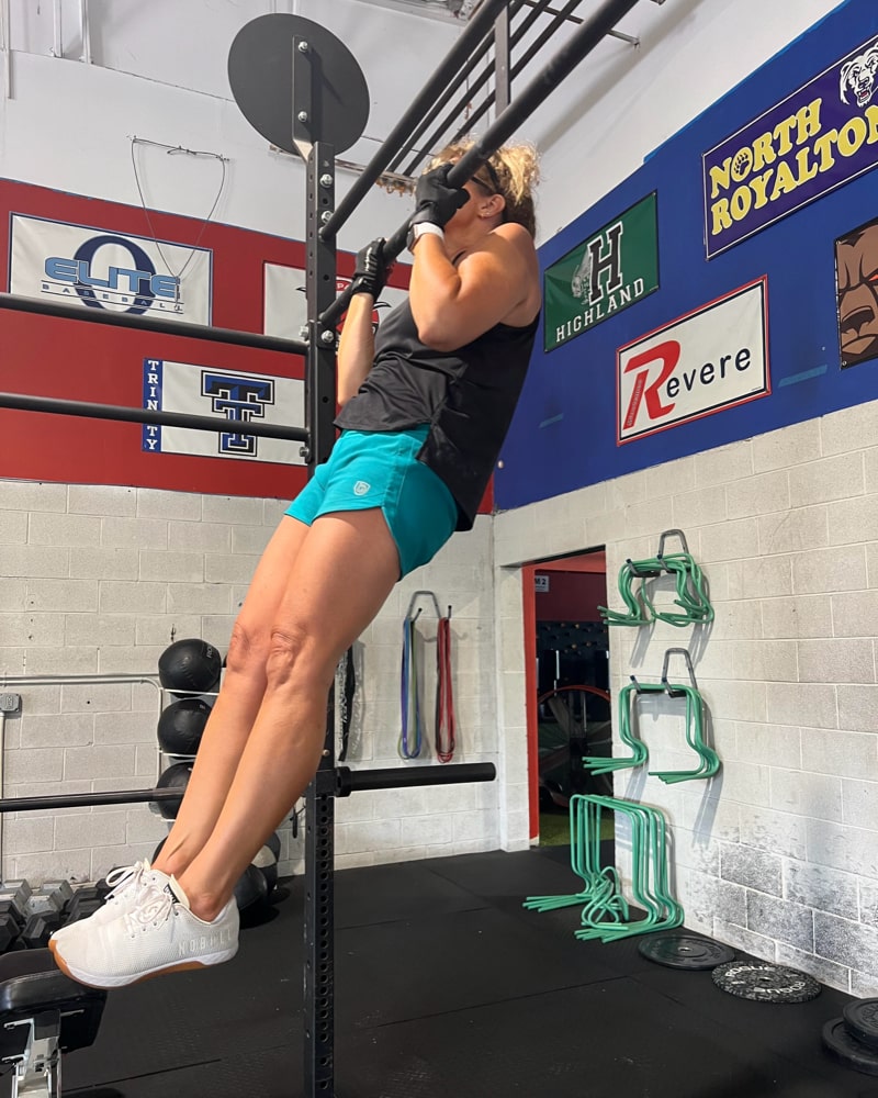 Person performing pull-ups in a gym setting with various logos on the wall.