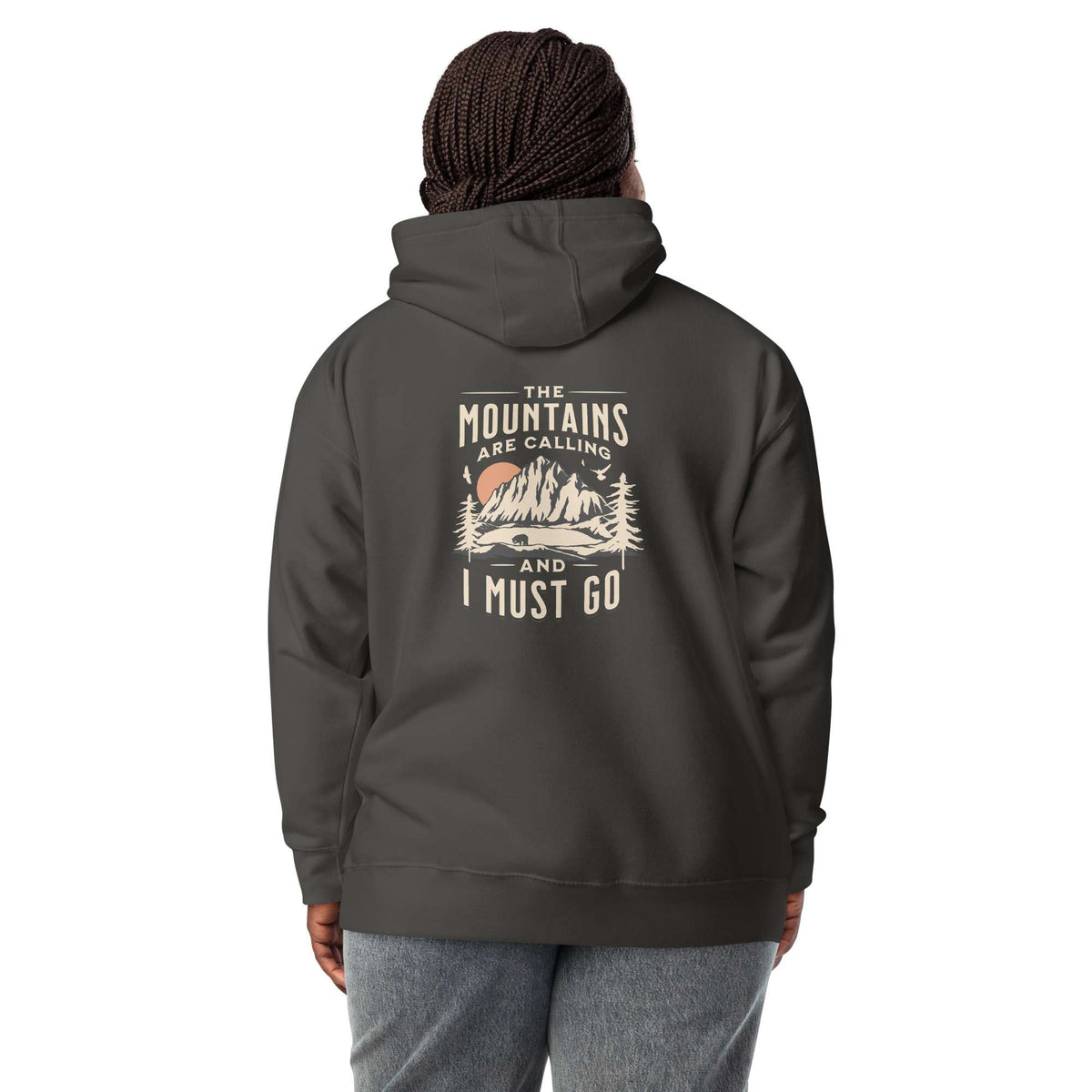 A person shown from the back wearing a dark charcoal gray hoodie with a vintage-style mountain graphic and the text 'THE MOUNTAINS ARE CALLING AND I MUST GO' printed on the back. The model is also wearing gray sweatpants against a plain white studio background. Nature Quote Mountains Are Calling Graphic Hoodie Casual Wear Shop the Nature Quote Mountains Are Calling Graphic Hoodie, a cozy statement piece for hikers, campers, and everyday adventure seekers.